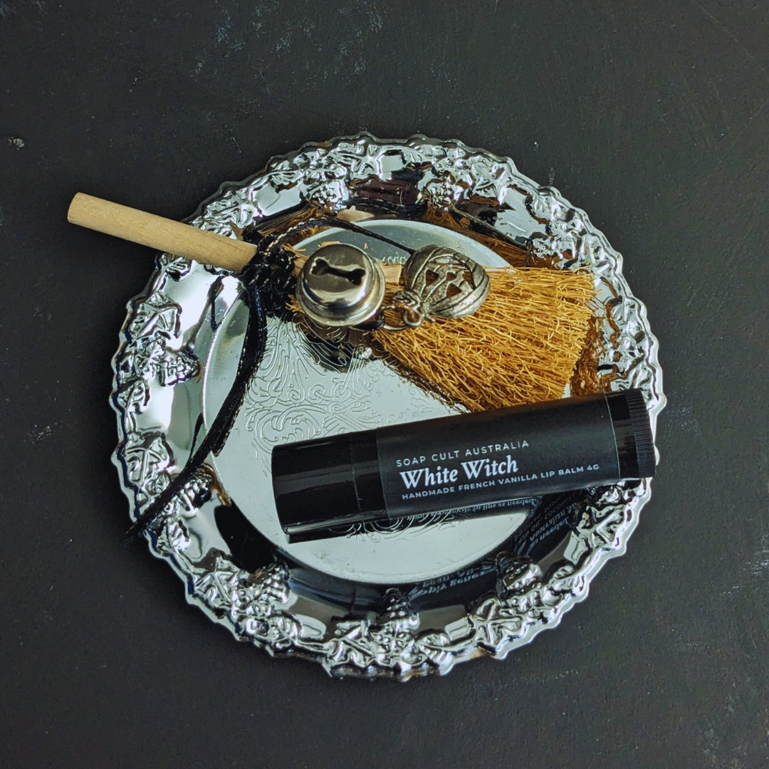 white witch lip balm on small silver tray with mini broomstick on mottled black surface