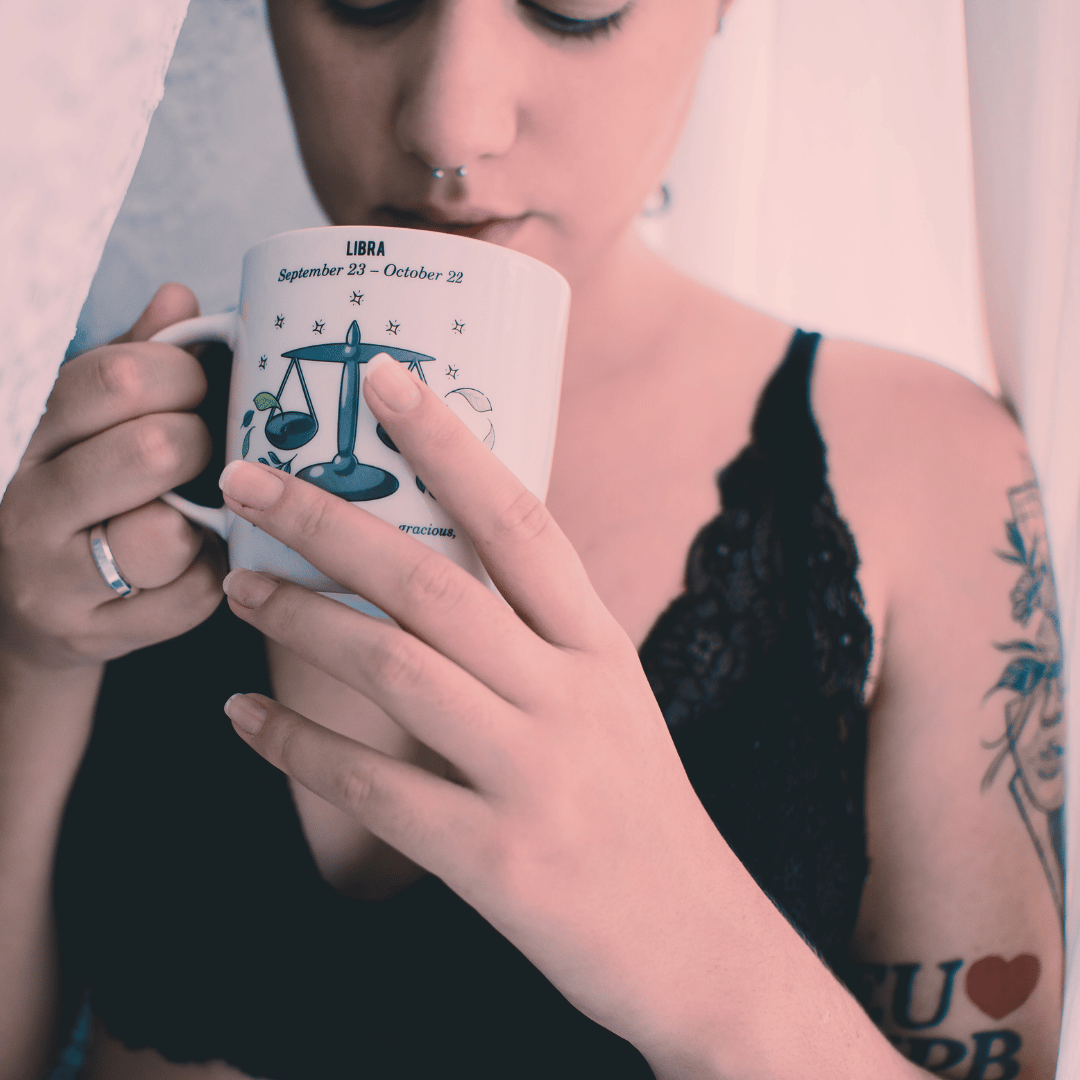 white person in black slip with tattoos drinking from libra coffee mug