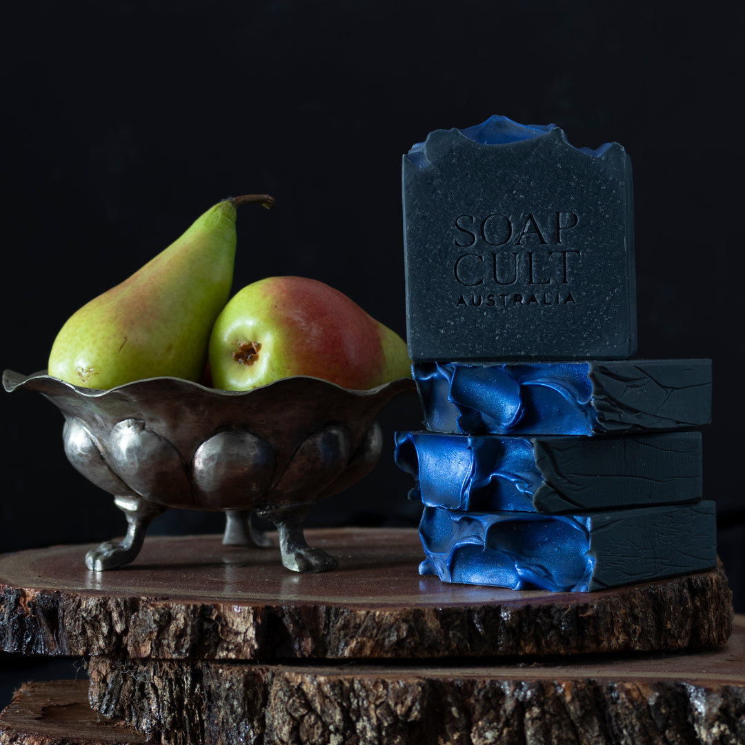 stacks of black and blue soap with bright pears in metal bowl with feet