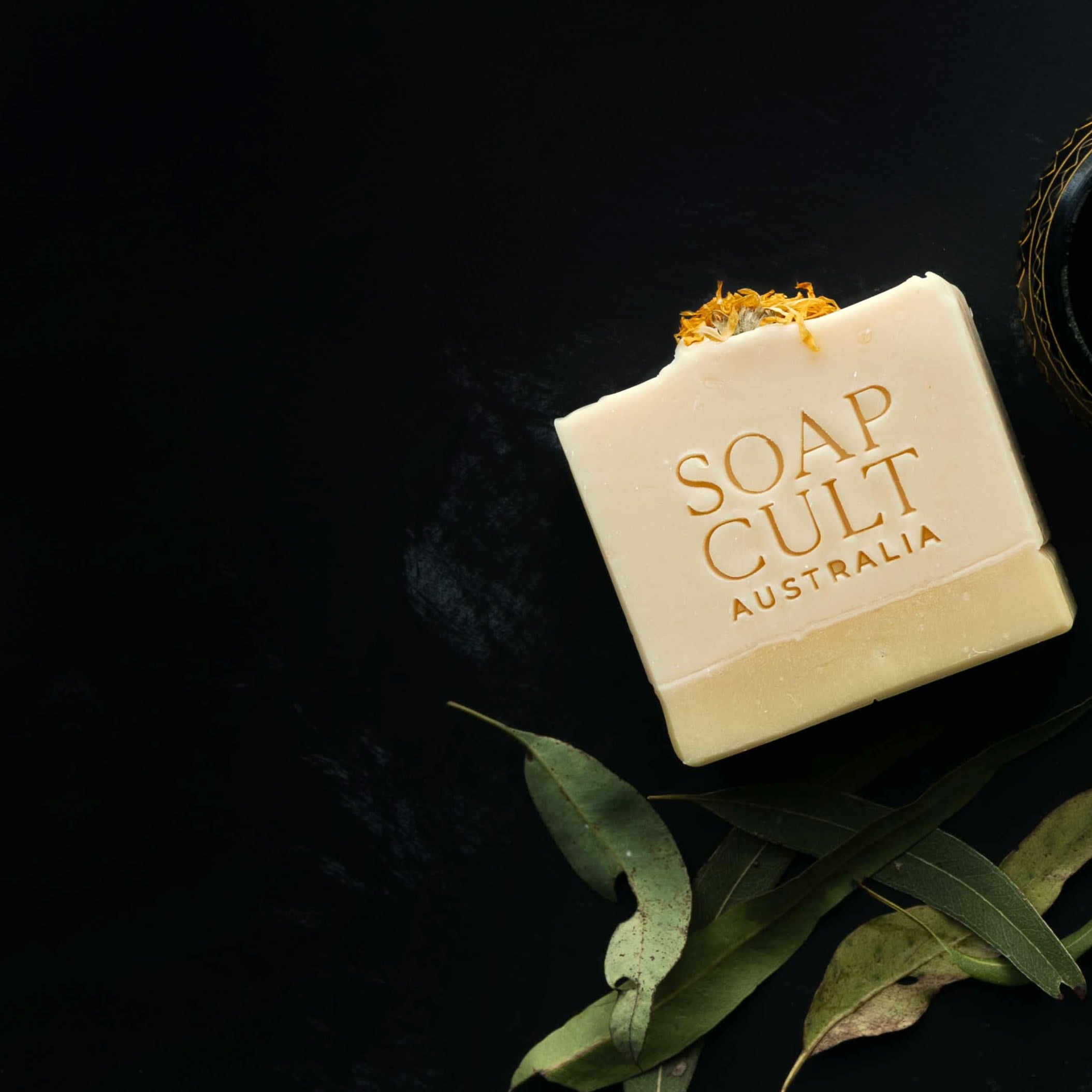 golden dawn lemon myrtle soap with caledula flower on black background with gum leaves