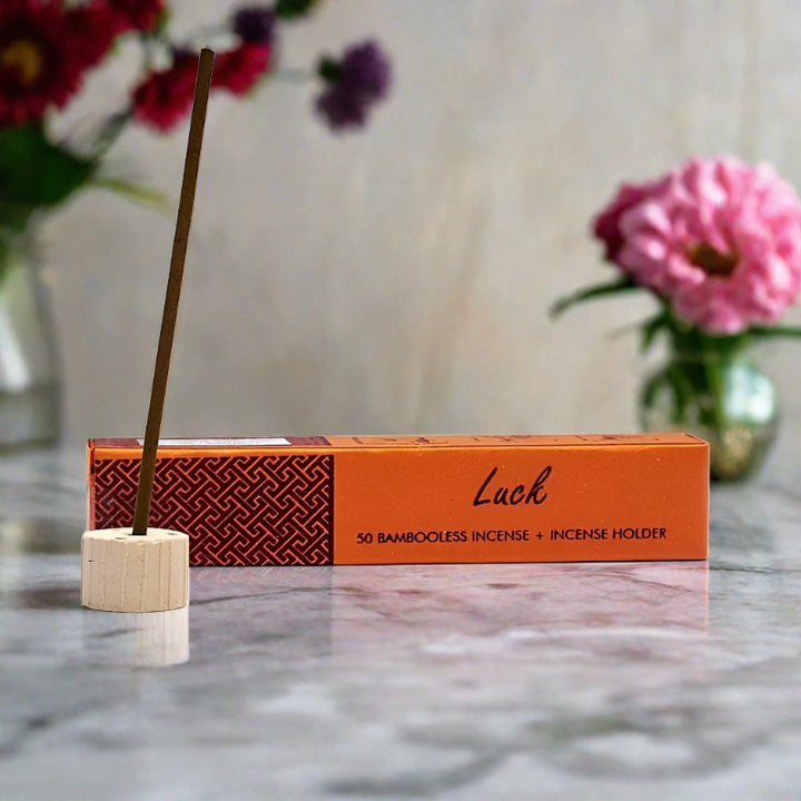 orange paper box with luck incense showing a stick in provided burner on white background