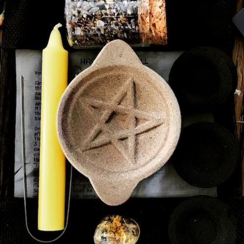 little pentagram stone holder near yellow wish candle and herbs in jar