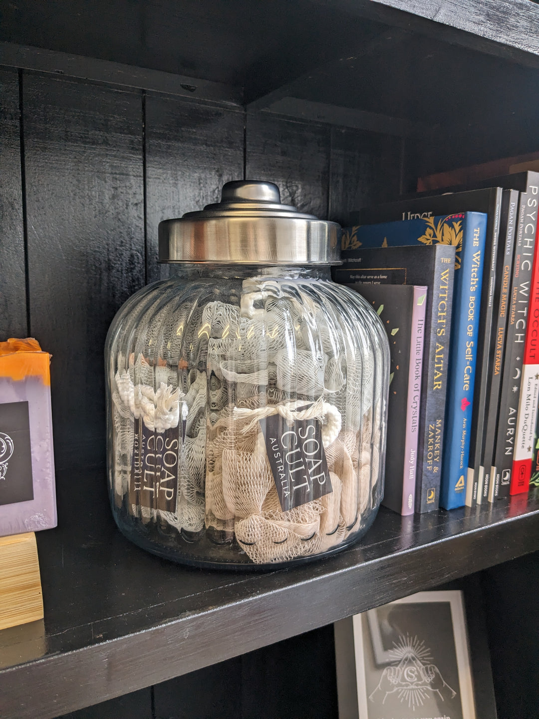 big ornate jar of shower puffs on black bookcase with witchcraft and occult books